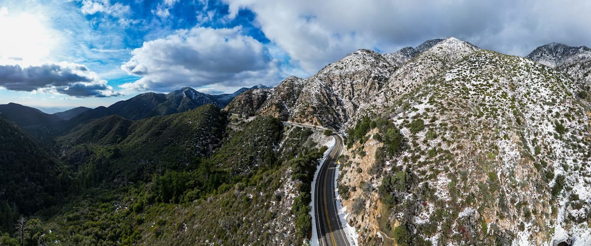 A mountainous landscape with a winding road, a waterfall, and snow-covered peaks.