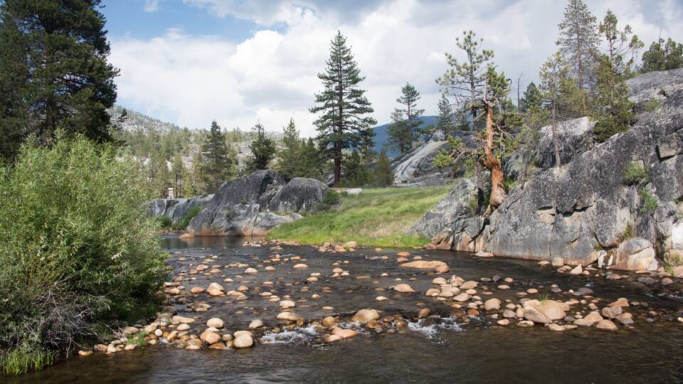 A river with large rocks, surrounded by trees and mountains.