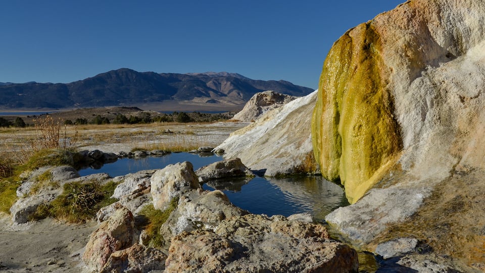 A geothermal area with hot springs, rocks, and mountains in the background.