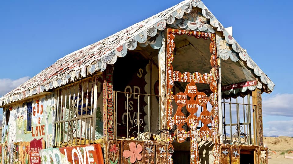 A colorful, weathered building with various decorations and signs, including 'God is Love' and 'GOD IS LOVE'.