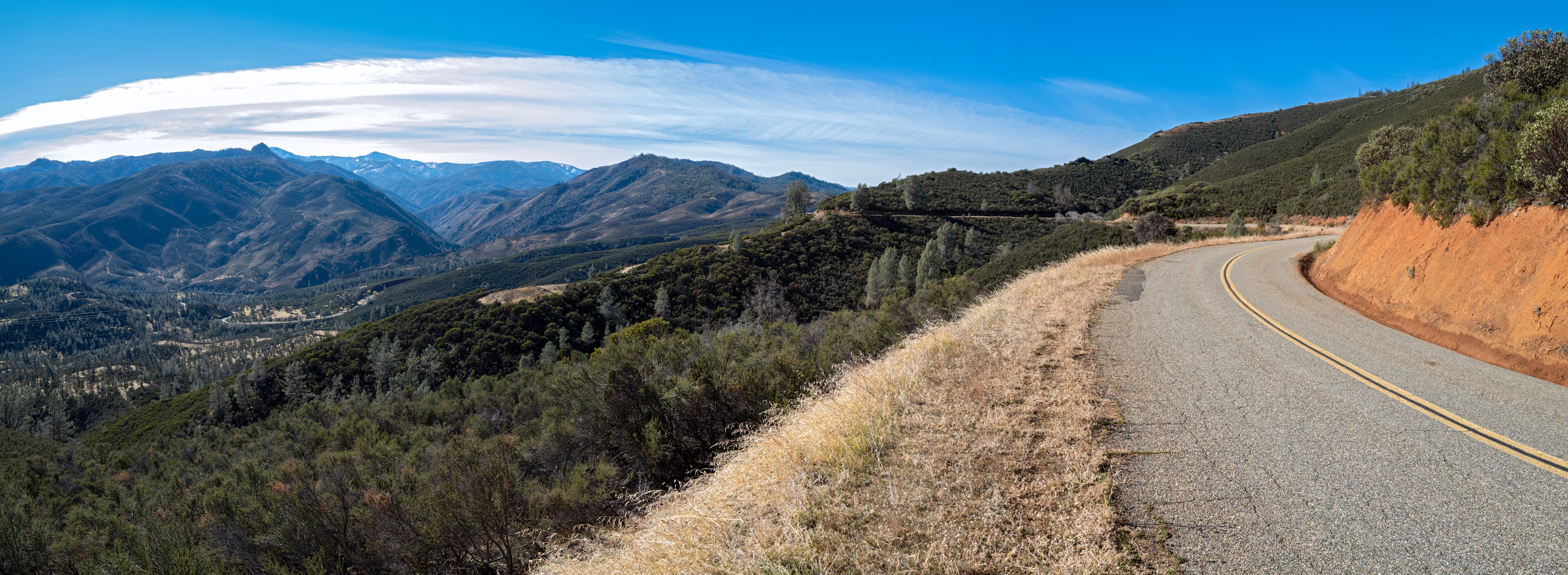 A winding mountain road with a clear blue sky and distant snow-capped peaks.