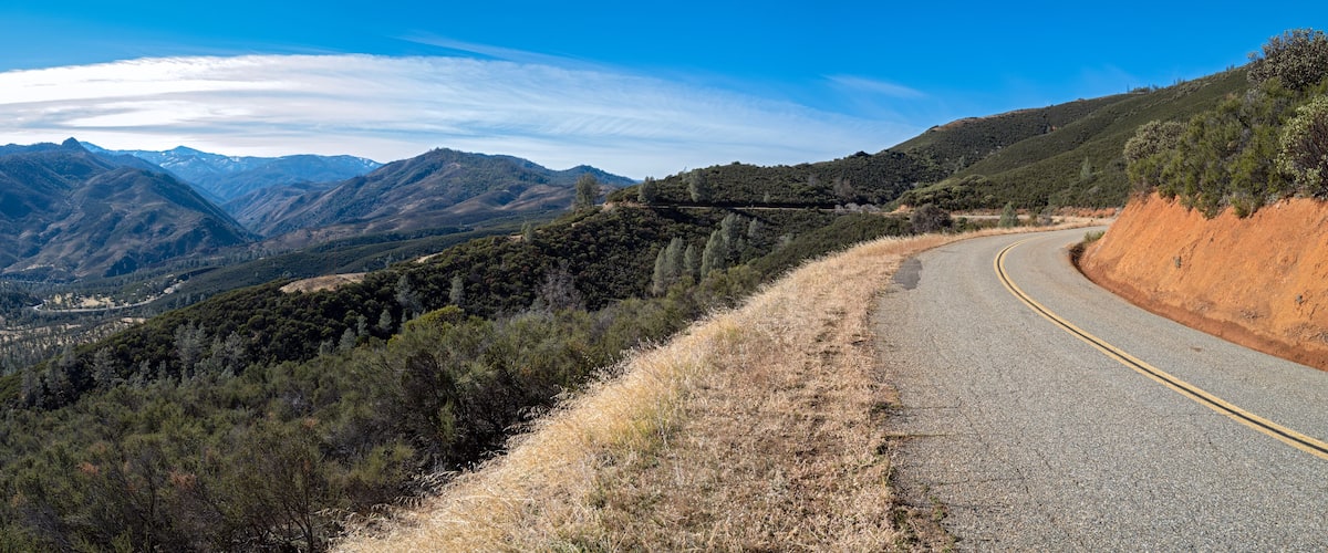 A winding mountain road with a clear blue sky and distant snow-capped peaks.