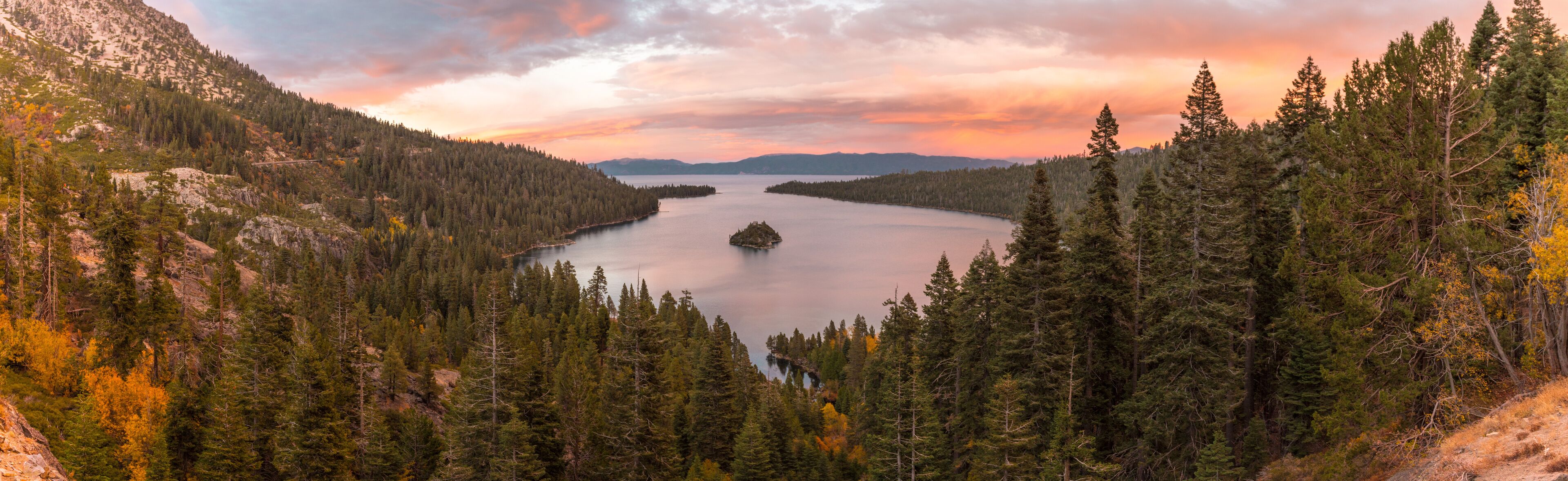 A lake surrounded by dense forests and mountains during sunset.