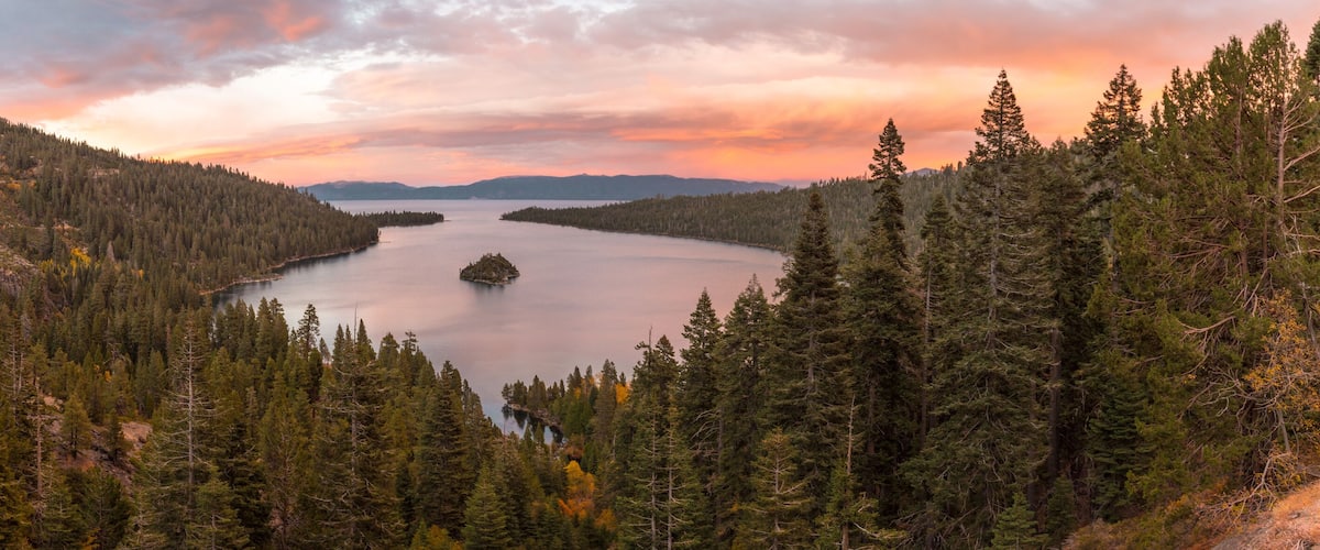 A lake surrounded by dense forests and mountains during sunset.