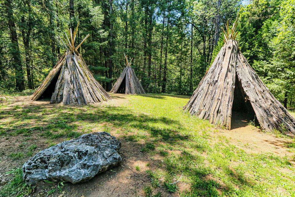 Three wooden teepees in a forest.