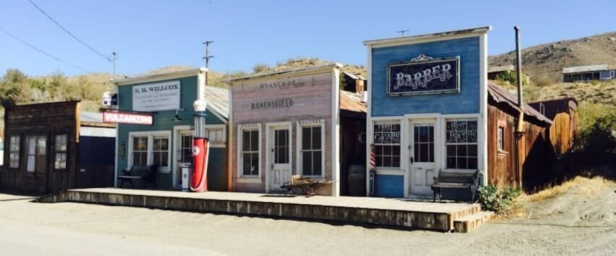 A row of old-fashioned buildings with signs for a barber, bakery, and other businesses.