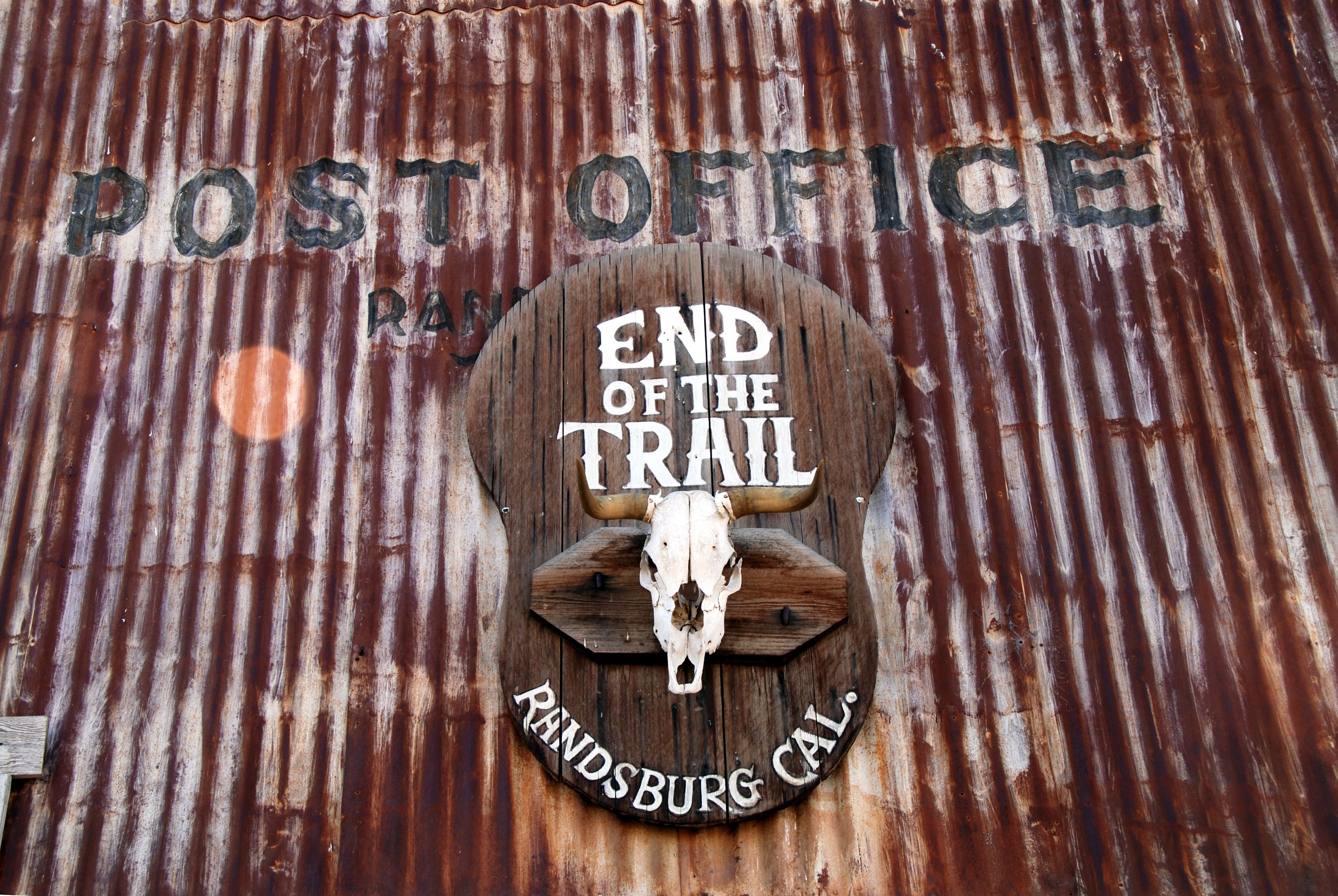 A rustic wooden sign with a cow skull, reading 'END OF THE TRAIL' and 'RHINDSBURG CAL.'
