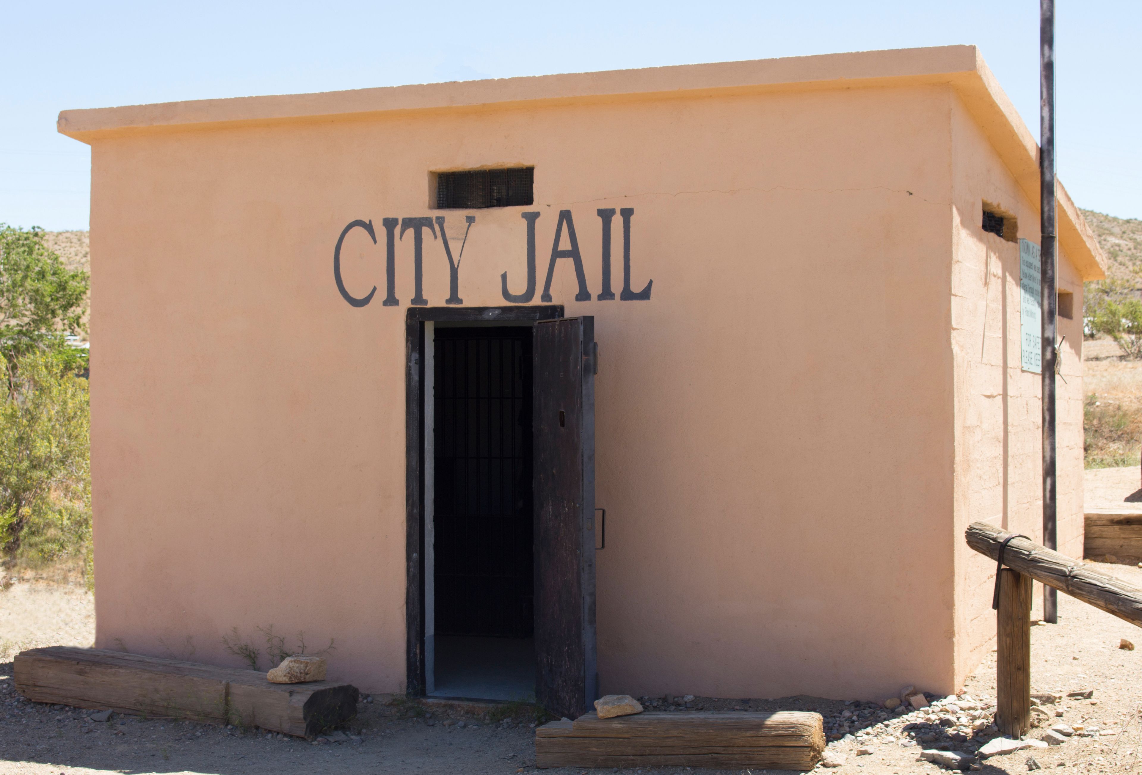 A small building labeled 'CITY JAIL' with a dark entrance and a wooden fence in front.