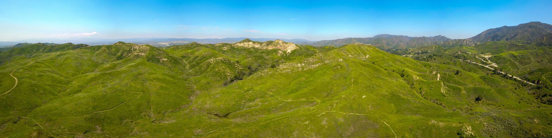 A mountainous landscape with winding roads and green hills under a clear blue sky.