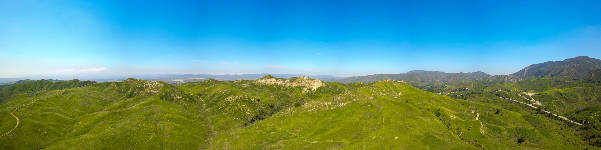Paisagem montanhosa com estradas sinuosas e colinas verdes sob um céu azul límpido.
