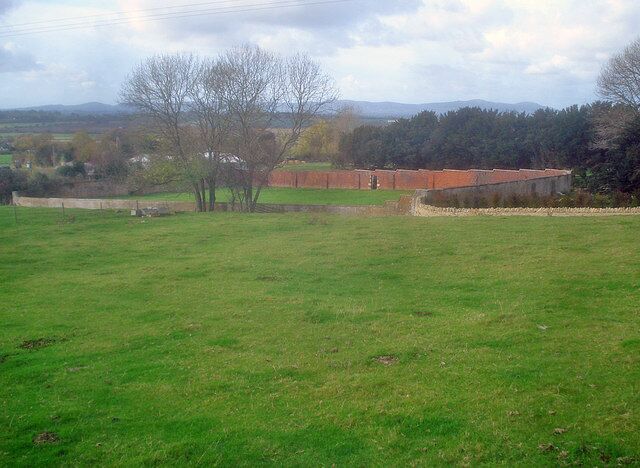 Um campo gramado com um edifício de tijolos e árvores ao fundo.