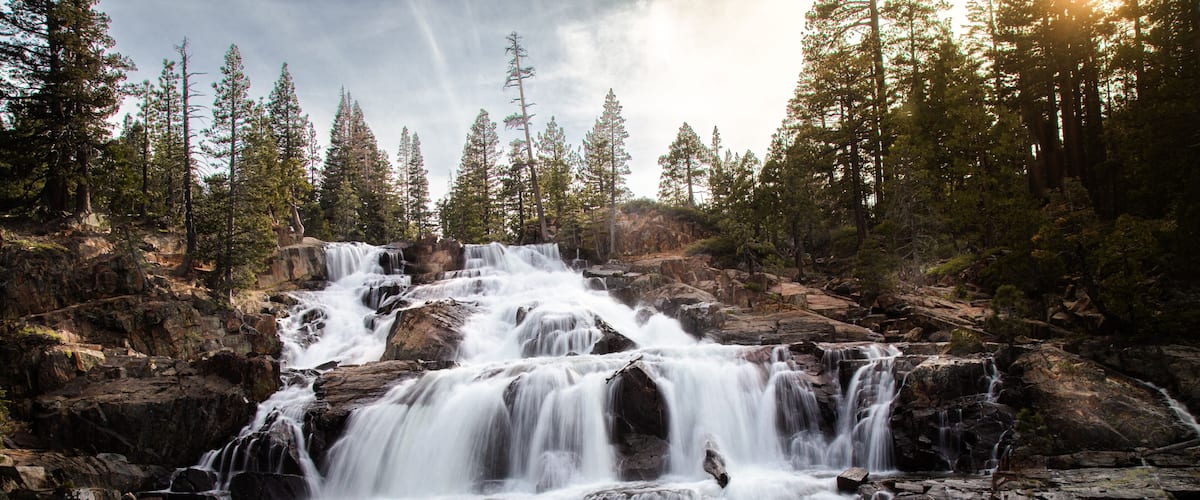 A multi-tiered waterfall surrounded by dense forest.