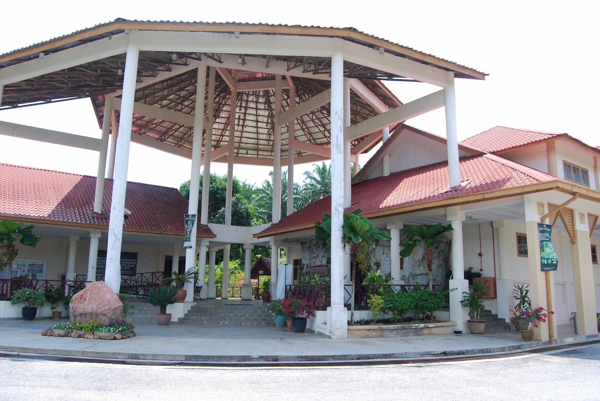 A covered pavilion with a tiled roof, surrounded by potted plants and a large rock centerpiece.