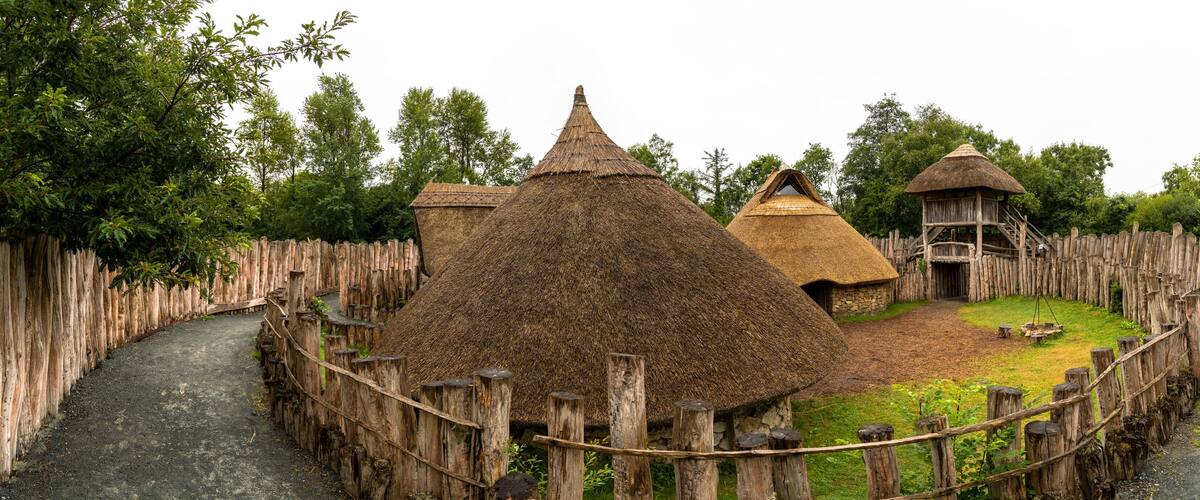 A rustic village with thatched-roof huts, wooden fences, and a central path.