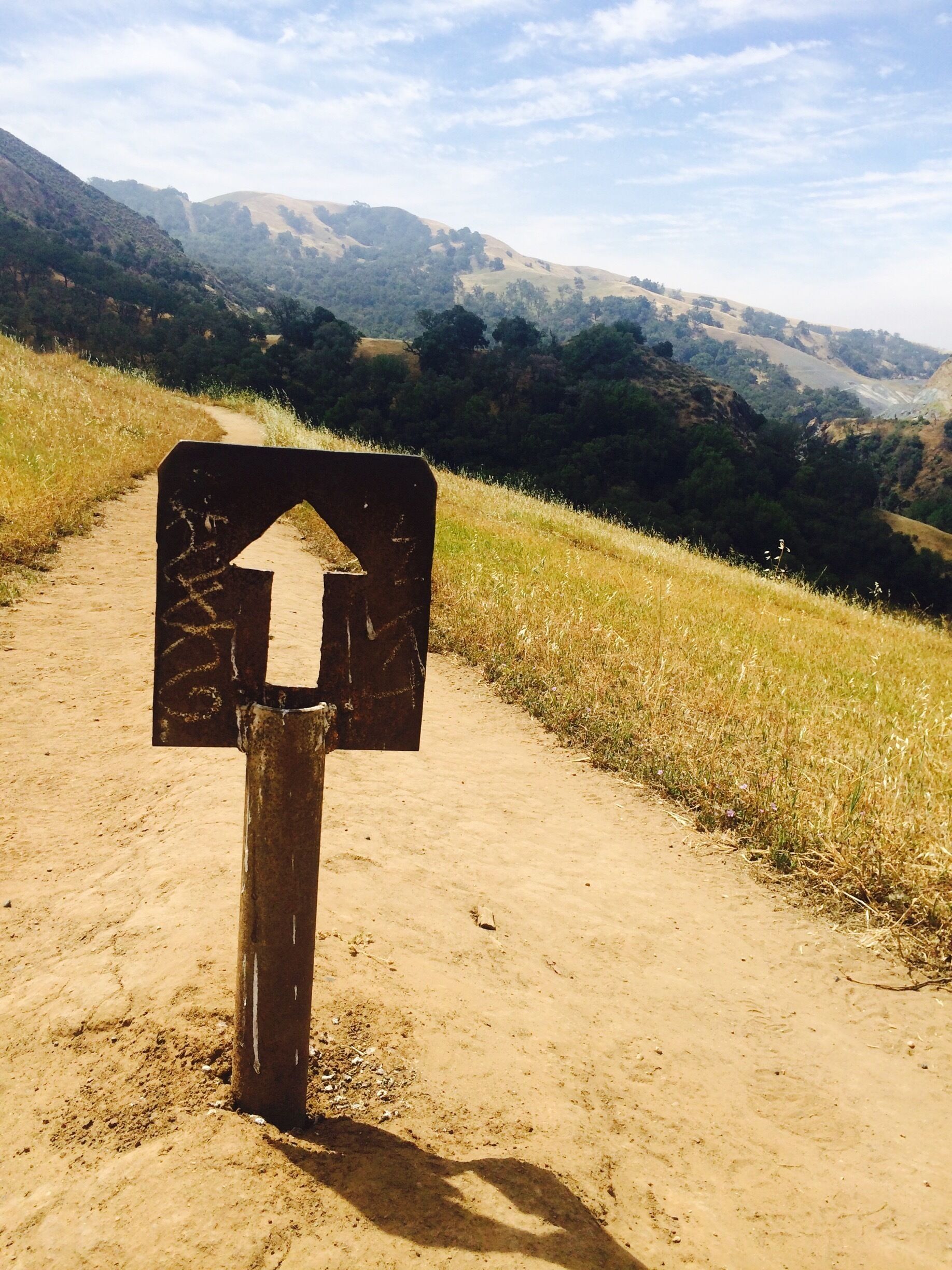 Un sendero de tierra con un cartel indicador y un paisaje montañoso al fondo.