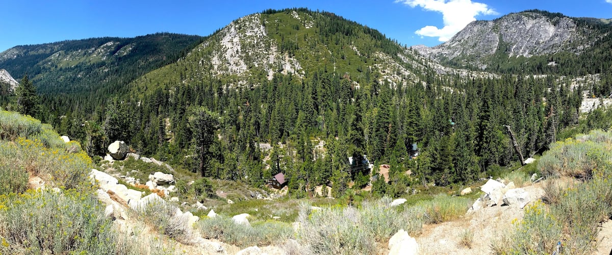 A mountainous landscape with dense forests, rocky outcrops, and a small cabin.
