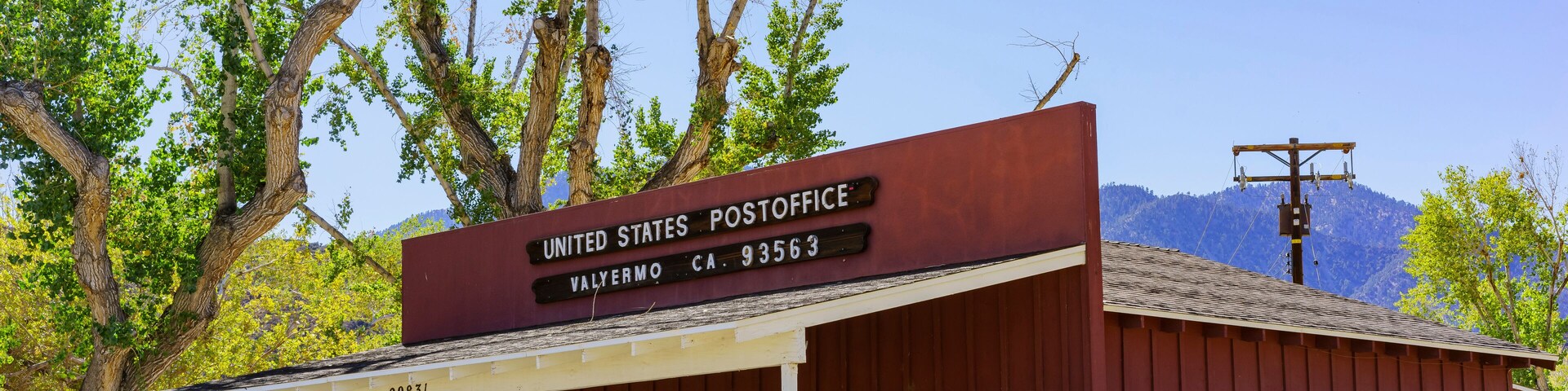 Un edificio rojo de correos de los Estados Unidos con un toldo blanco, ubicado en Valyermo, CA 93563.