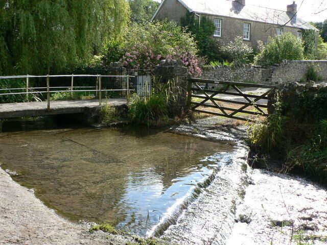 A small stream with a wooden bridge and a stone wall.