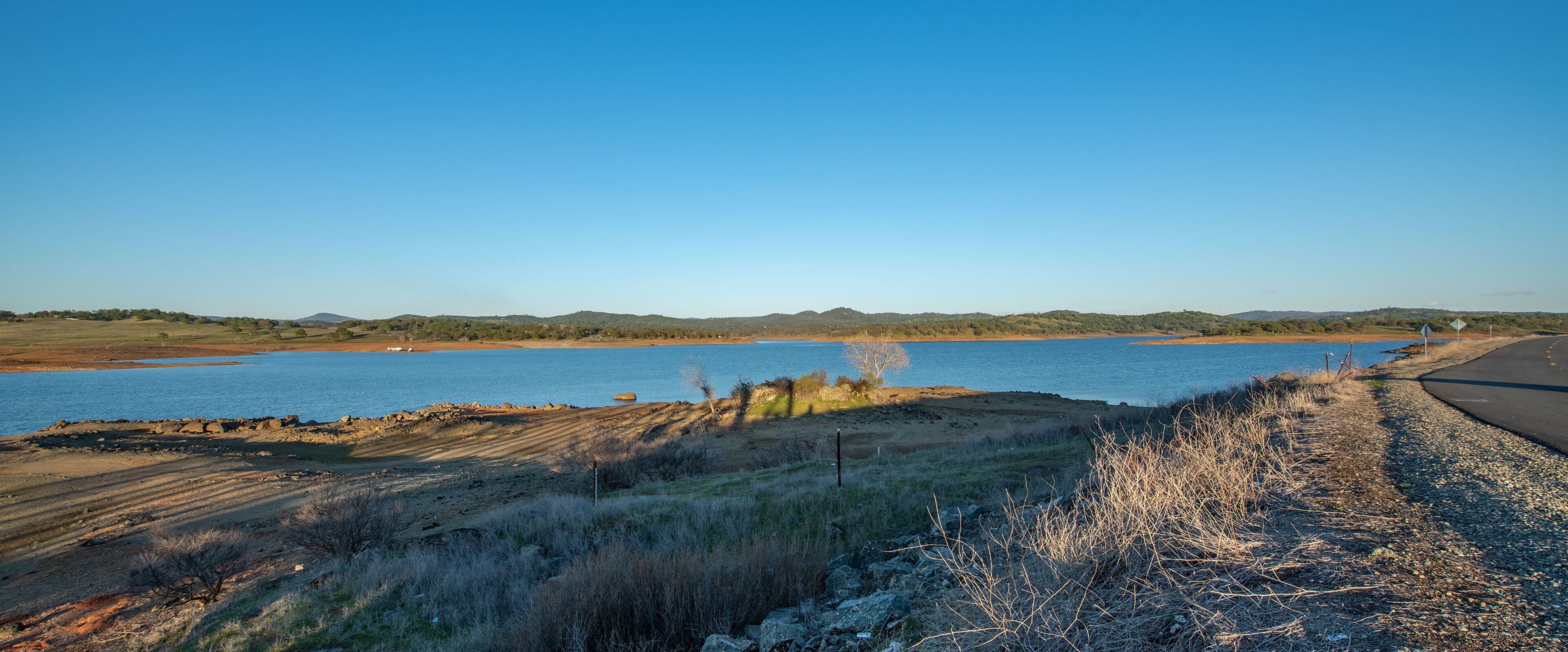 A coastal landscape with a body of water, a dirt path, and distant hills.