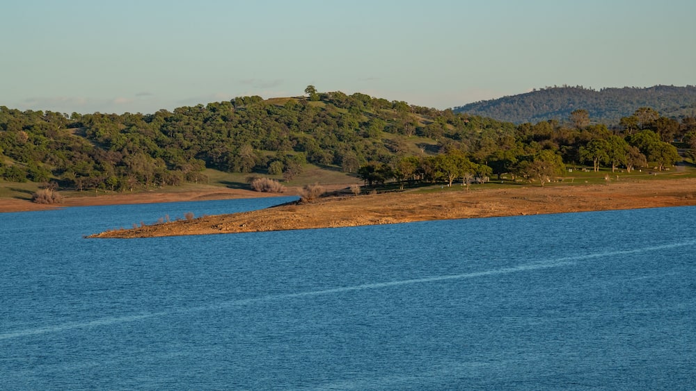 A calm lake with a small island in the center, surrounded by hills with dense forests.