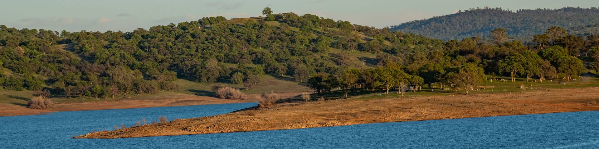 A calm lake with a small island in the center, surrounded by hills with dense forests.