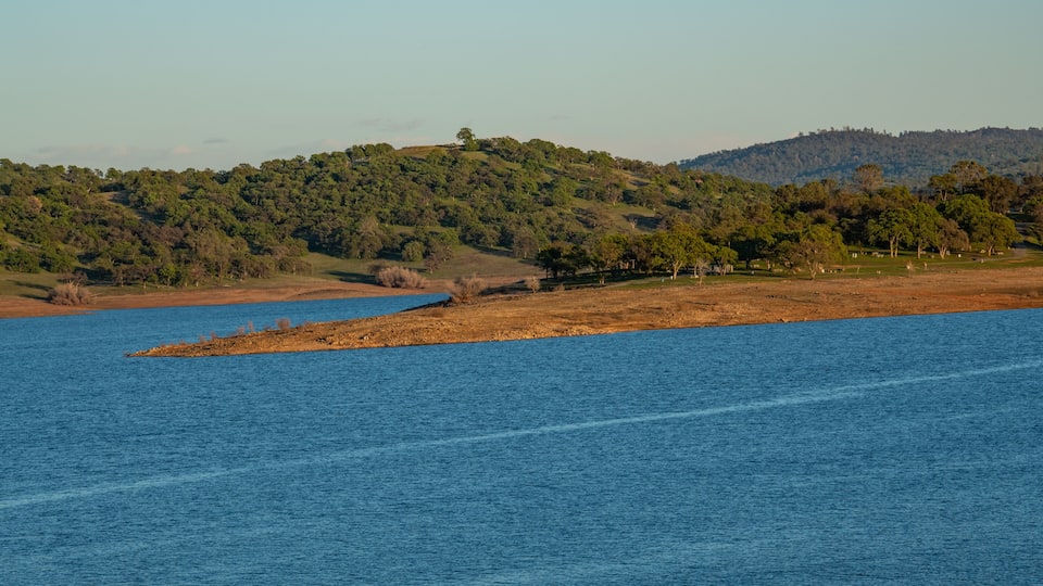 A calm lake with a small island in the center, surrounded by hills with dense forests.