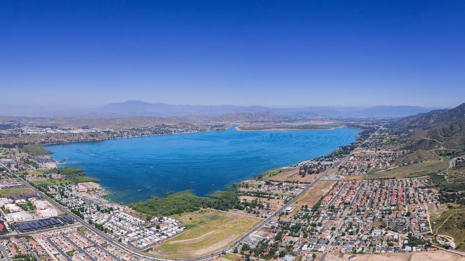 An aerial view of a coastal city with a large bay, residential areas, and hilly terrain.