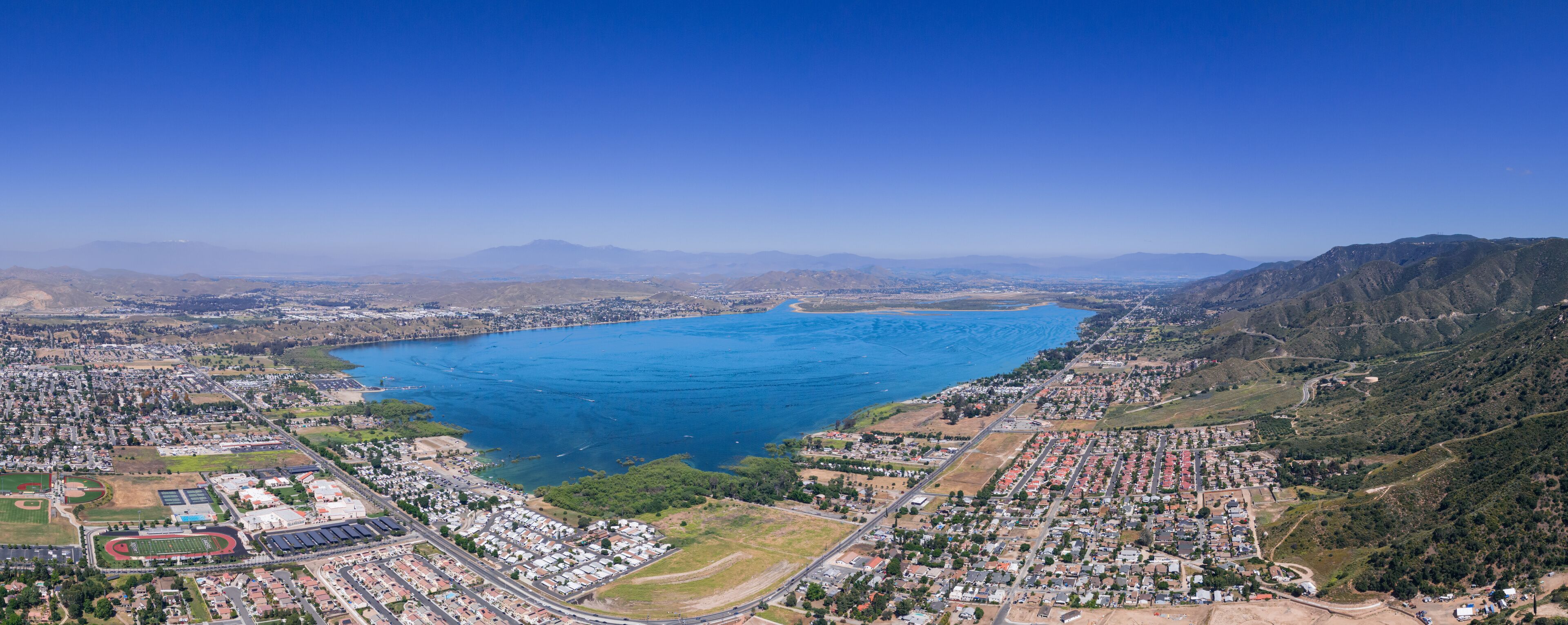 An aerial view of a coastal city with a large bay, residential areas, and hilly terrain.