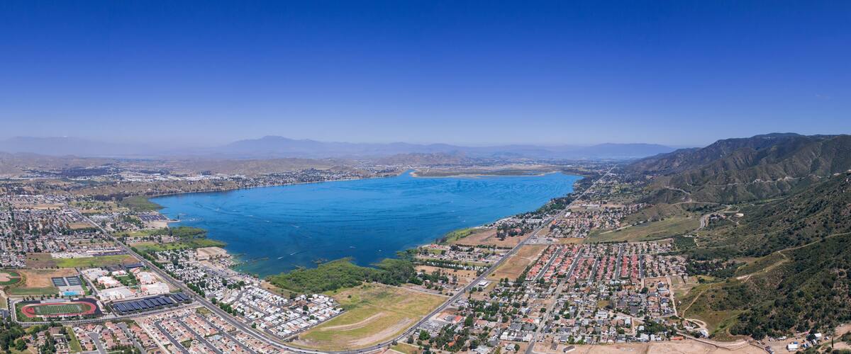 An aerial view of a coastal city with a large bay, residential areas, and hilly terrain.