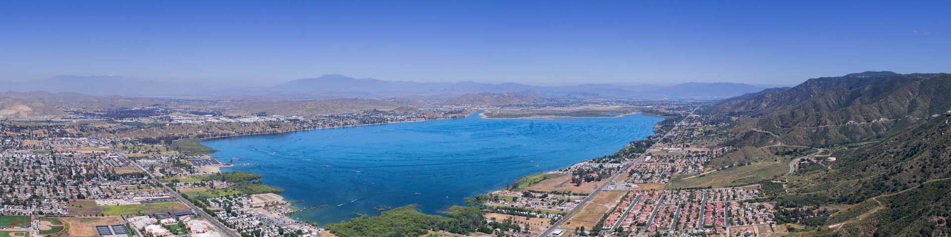 An aerial view of a coastal city with a large bay, residential areas, and hilly terrain.
