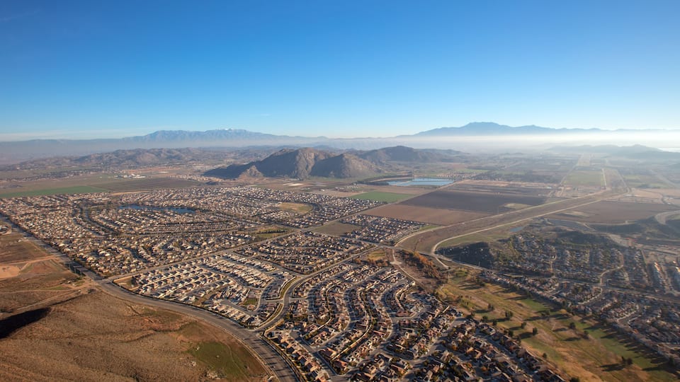 An aerial view of a densely populated urban area with a river, surrounding mountains, and a clear sky.