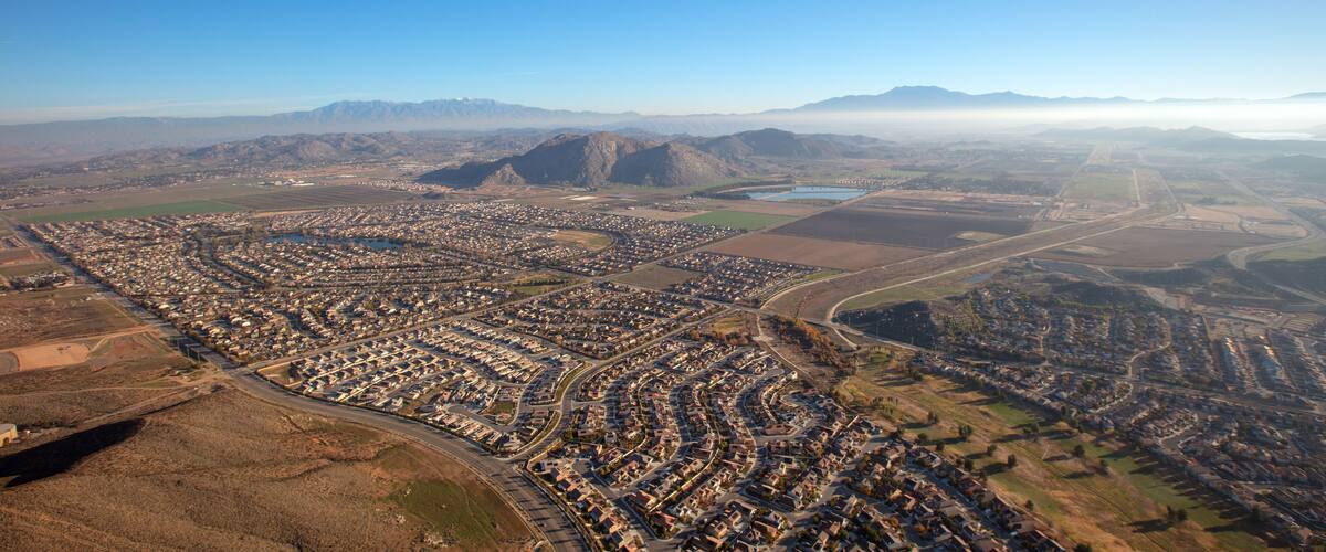 An aerial view of a densely populated urban area with a river, surrounding mountains, and a clear sky.