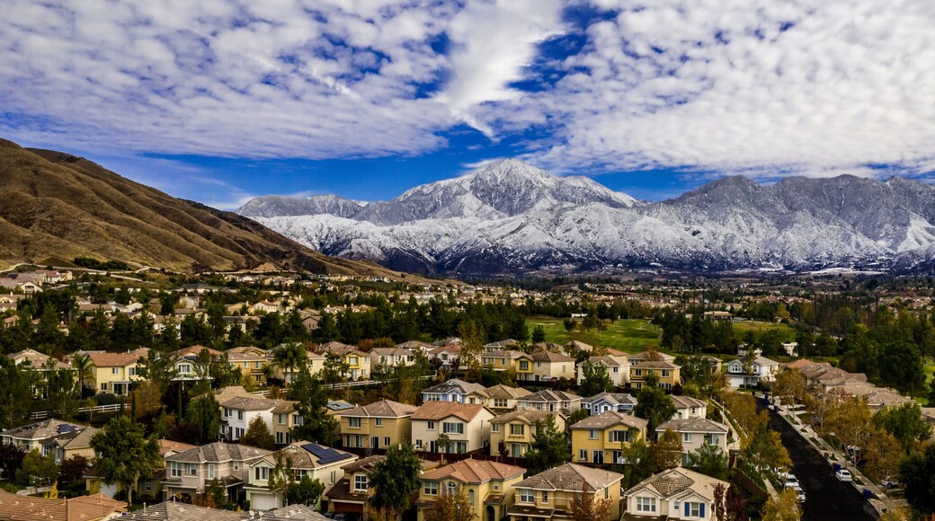 Aerial panorama of snow covered San Gorgonio and Little San Bernardino Mountains on a winter day above Yucaipa Valley with blue sky, white clouds, houses, hills