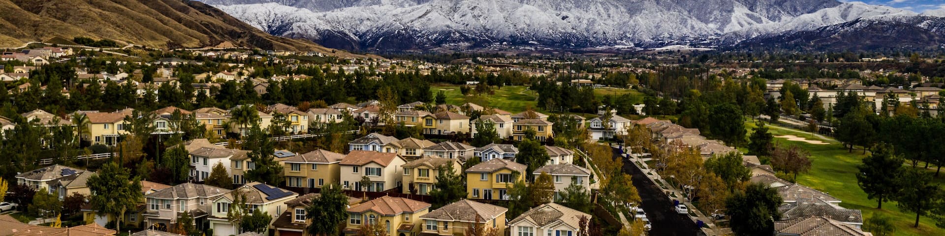 Aerial panorama of snow covered San Gorgonio and Little San Bernardino Mountains on a winter day above Yucaipa Valley with blue sky, white clouds, houses, hills