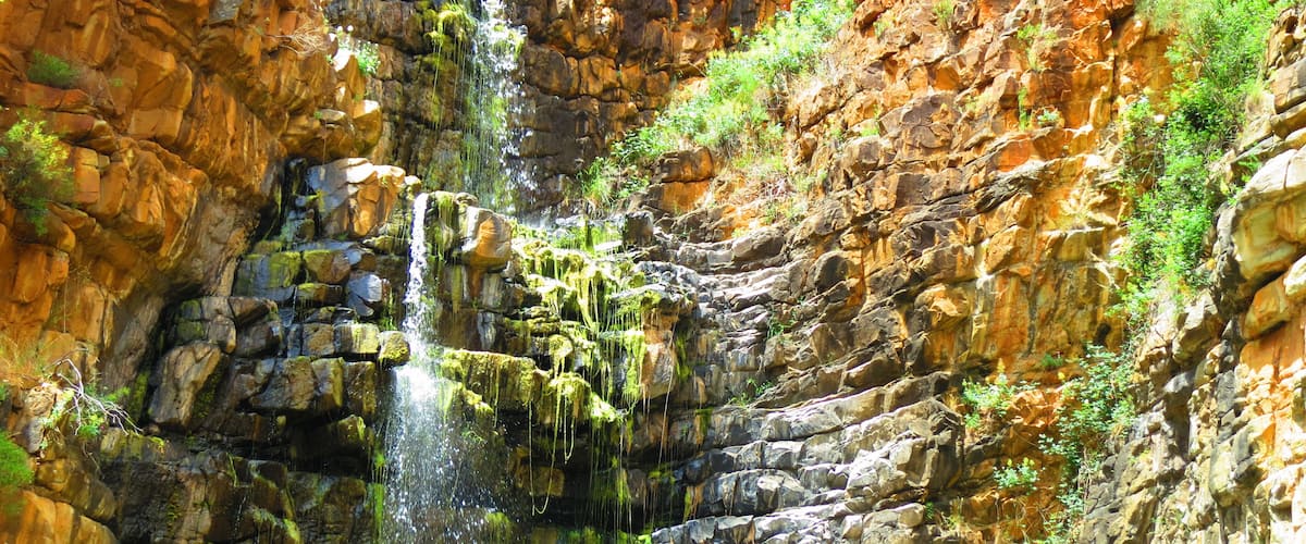 A waterfall cascading down a rocky cliff with moss-covered rocks and greenery.
