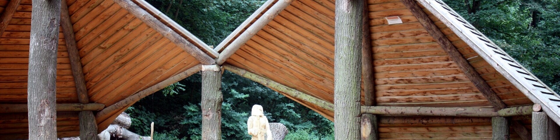 Two wooden structures with triangular roofs, surrounded by trees and logs.
