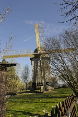 A windmill in a grassy field with trees and a wooden fence.