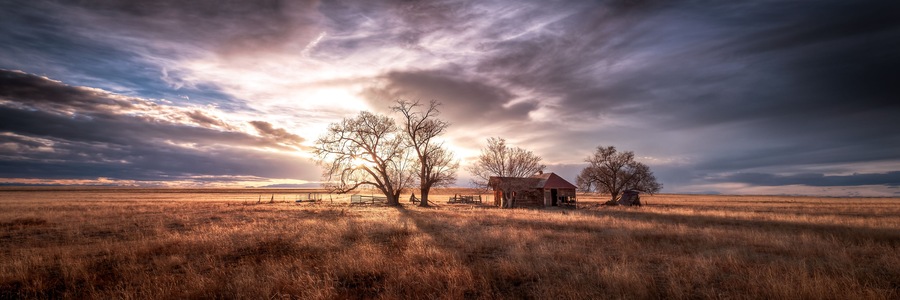 An old farmhouse on the eastern plains of Colorado in a rural setting at sunset. The sky is dramatic with wispy clouds. The old house if falling apart and abandoned.