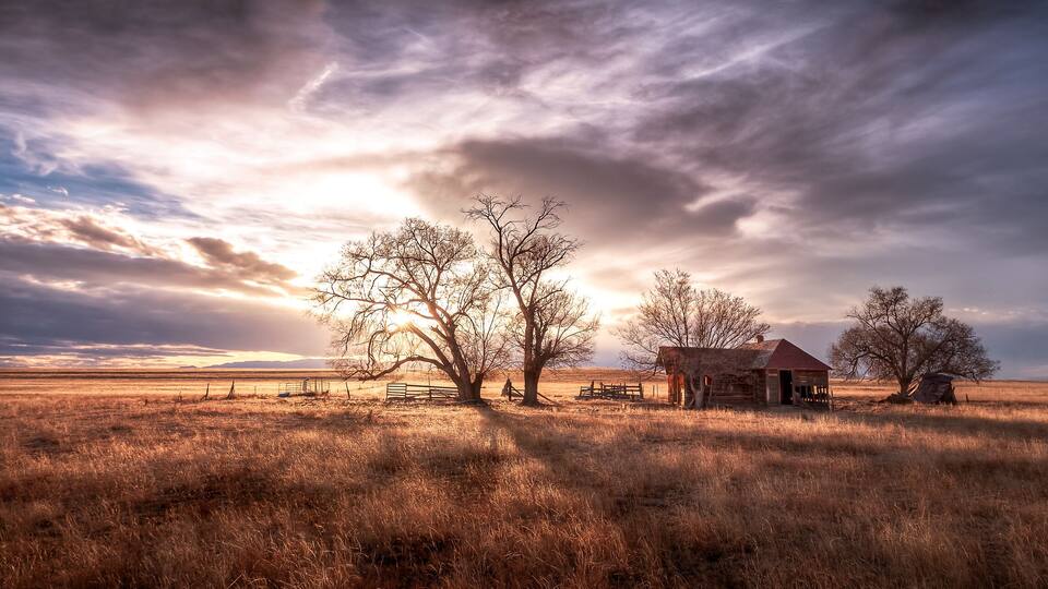 A rural landscape with a barn, trees, and a fence.
