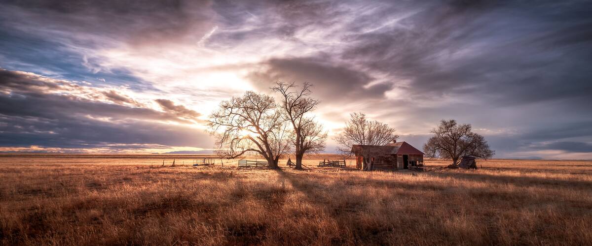 A rural landscape with a barn, trees, and a fence.