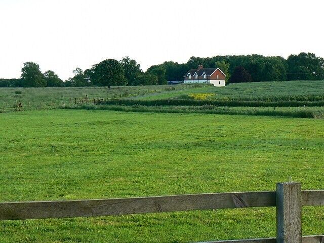 A green field with a wooden fence in the foreground and a house in the background.