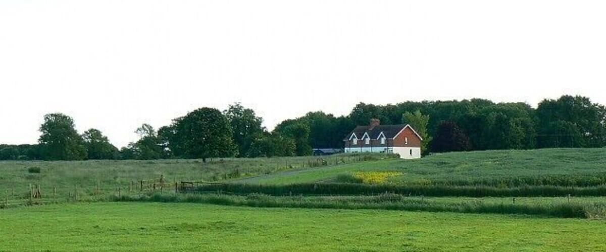 A green field with a wooden fence in the foreground and a house in the background.