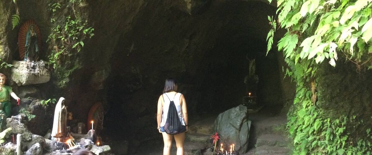 A cave entrance with a statue, a woman standing, and a fire pit.