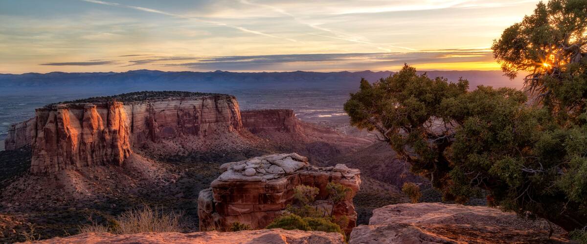 A canyon landscape with prominent rock formations and a sunset in the background.