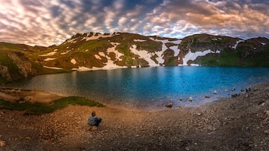 Un lac de montagne parsemé de plaques de neige, avec des rives rocheuses et un ciel nuageux.