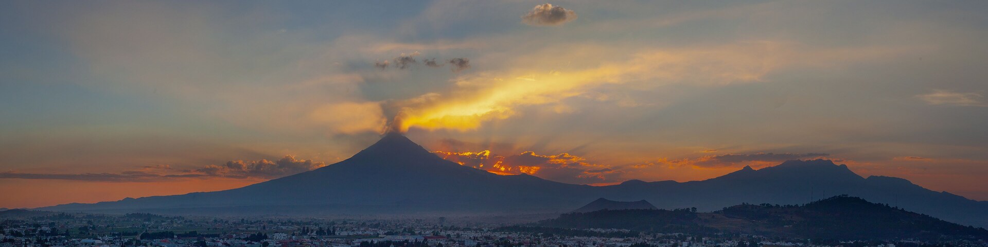 Um vulcão em erupção, com uma cidade ao primeiro plano.