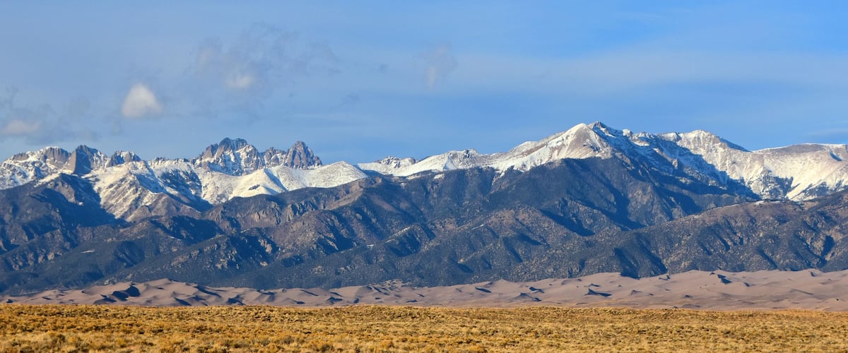 A mountain range with snow-capped peaks and a desert landscape in the foreground.