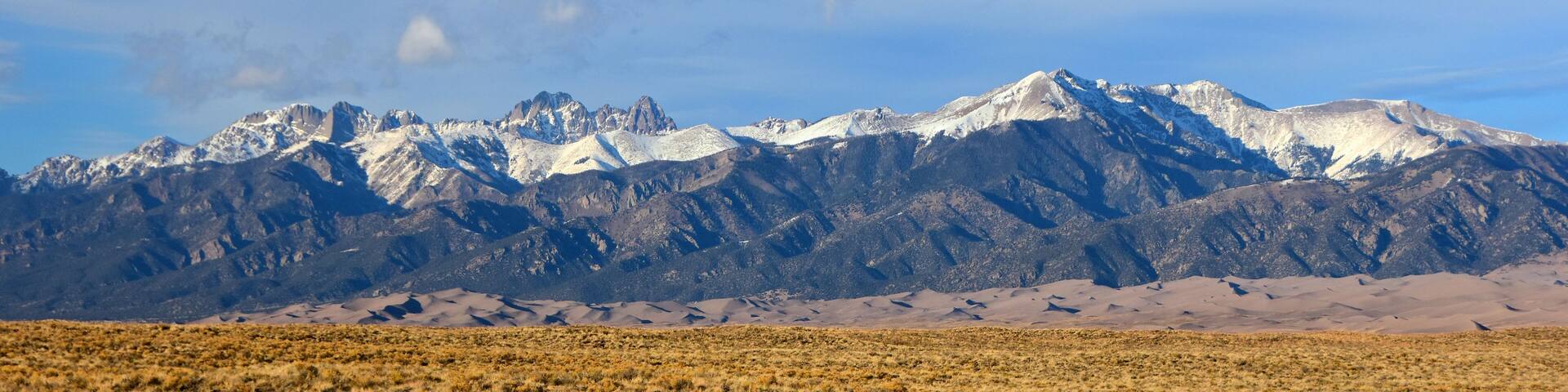 A mountain range with snow-capped peaks and a desert landscape in the foreground.
