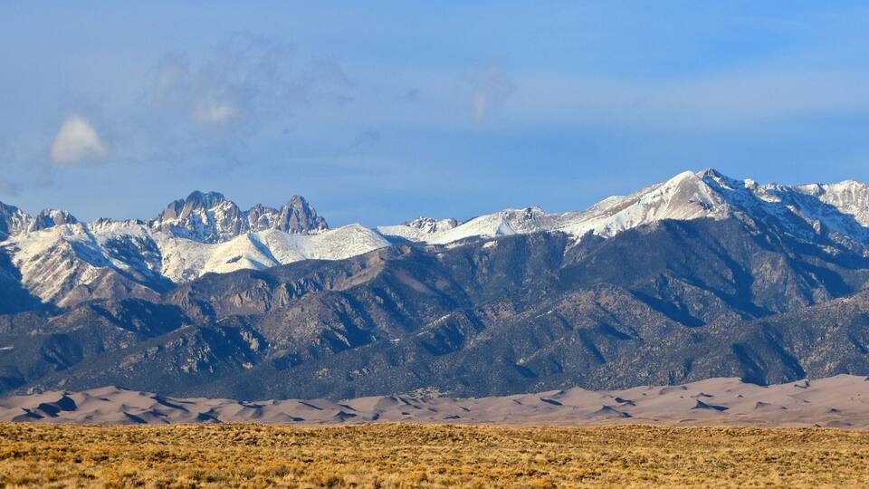 A mountain range with snow-capped peaks and a desert landscape in the foreground.