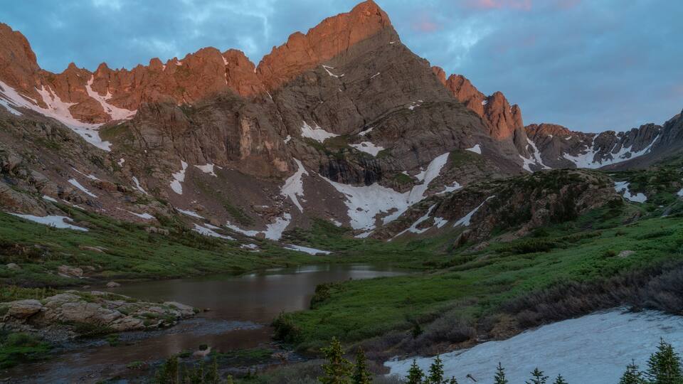 A mountain range with a lake and snow patches.